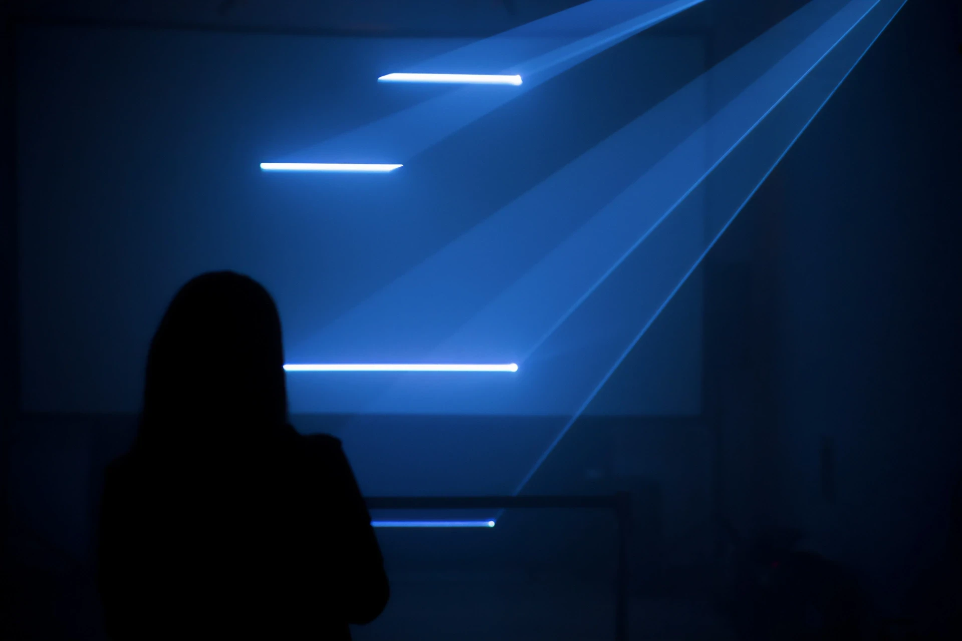 Silhouette of a person facing blue light beams.