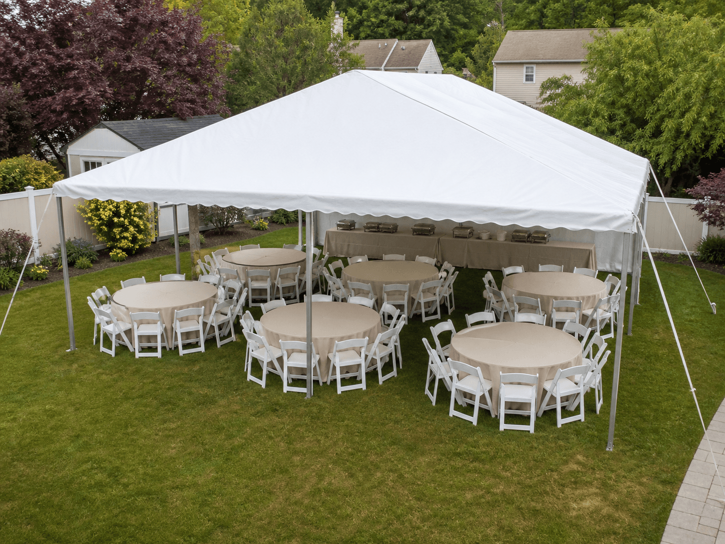 Frame tent shading round banquet tables and white folding chairs in a backyard