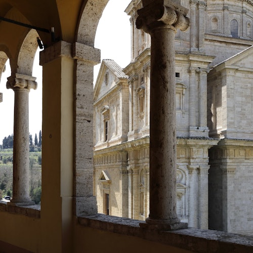 透過一系列拱門觀賞一座歷史悠久的石建築，前景有柱子，背景可見一幅風景。