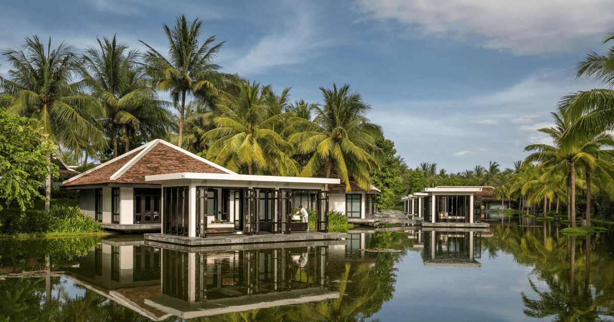 A resort surrounded by palm trees and calm reflective water.