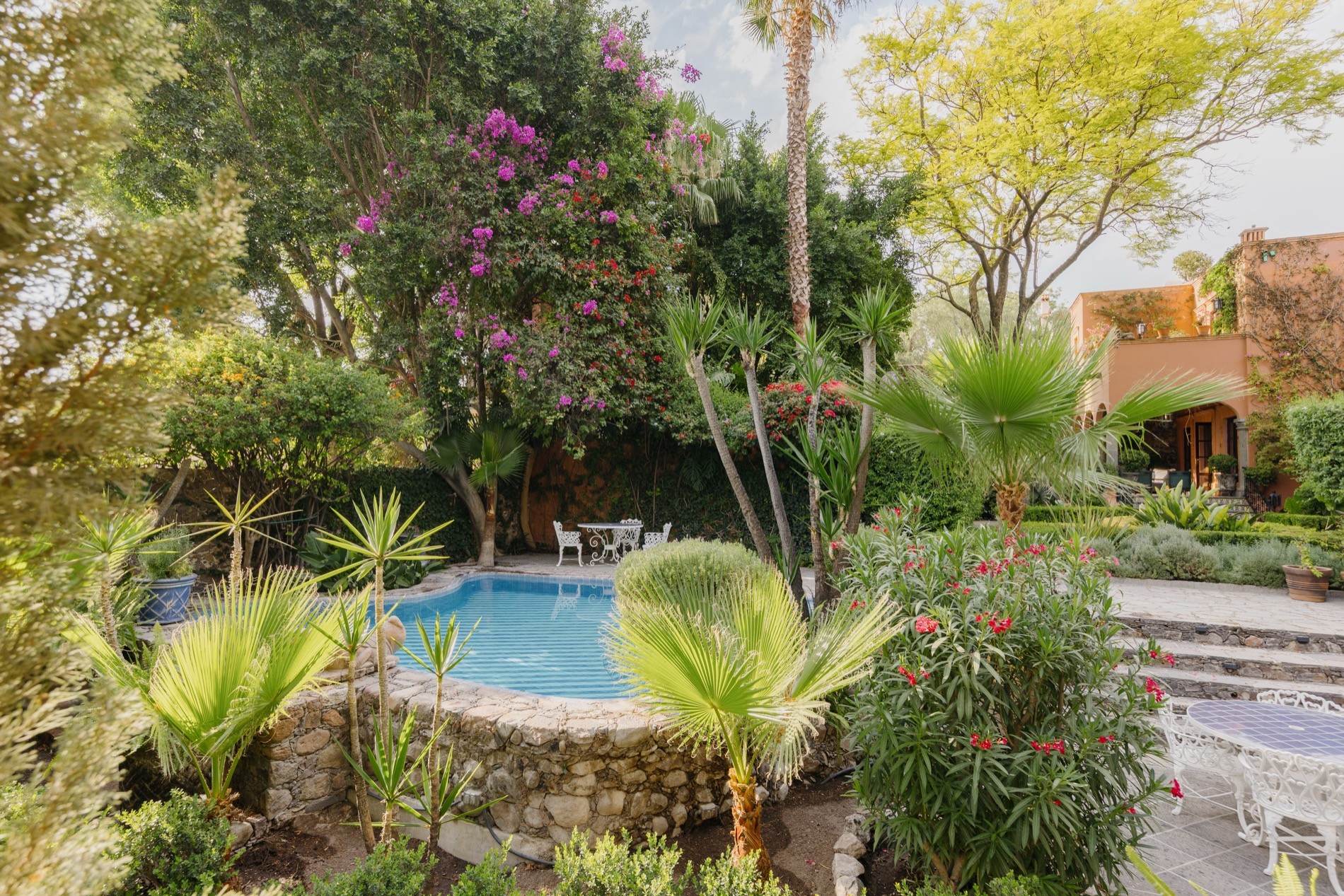 La Residencia San Miguel pool framed by tropical palms and bougainvillea with poolside seating
