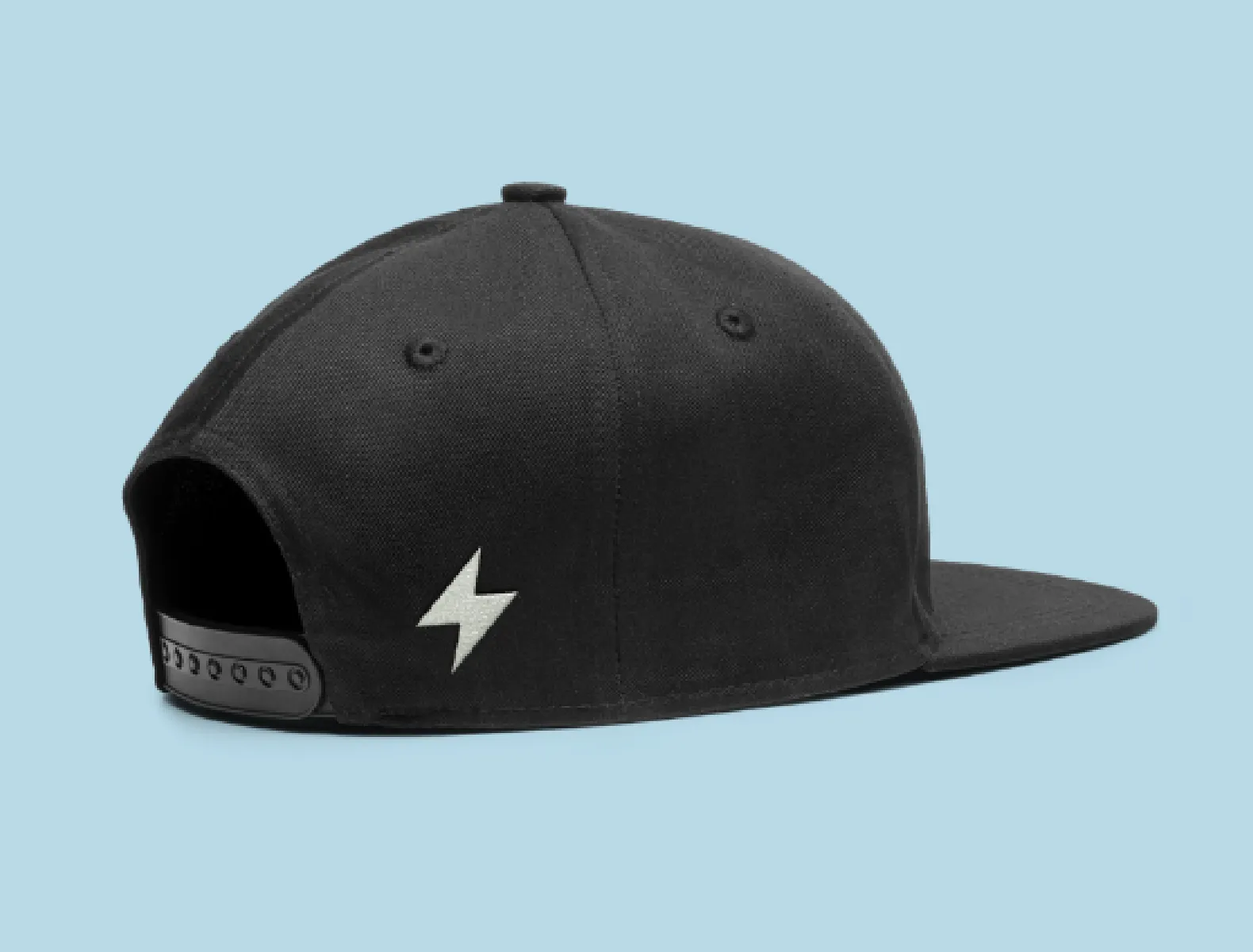 A lightning bolt embroidered on the back side of a black flat brimmed hat on a sky blue background.