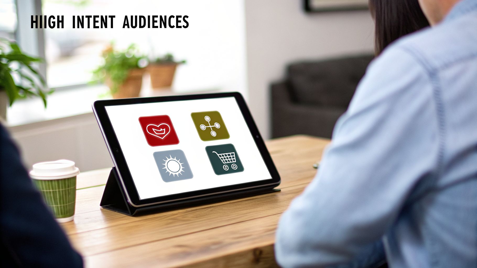 Digital tablet showing icons for high-intent audiences like love, network, weather, and shopping, during a business meeting.