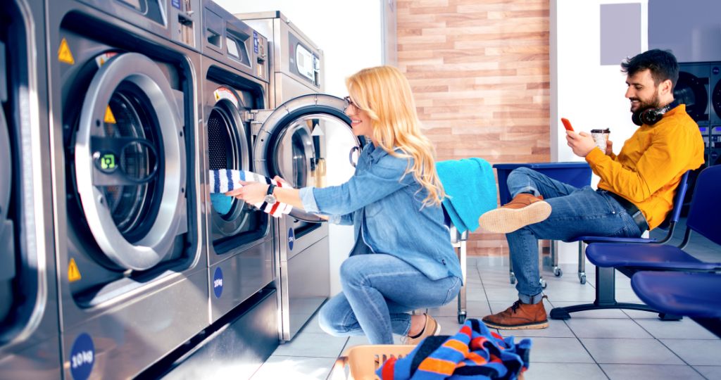 Laundromat customer loading laundry as another sits on their phone