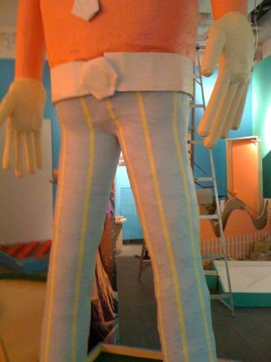 a man statue with blue trousers with vertical yellow lines and an orange shirt
