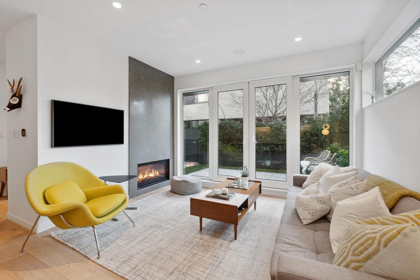 Bright living room with large windows, a yellow chair, a comfortable sofa, and a wall-mounted TV.
