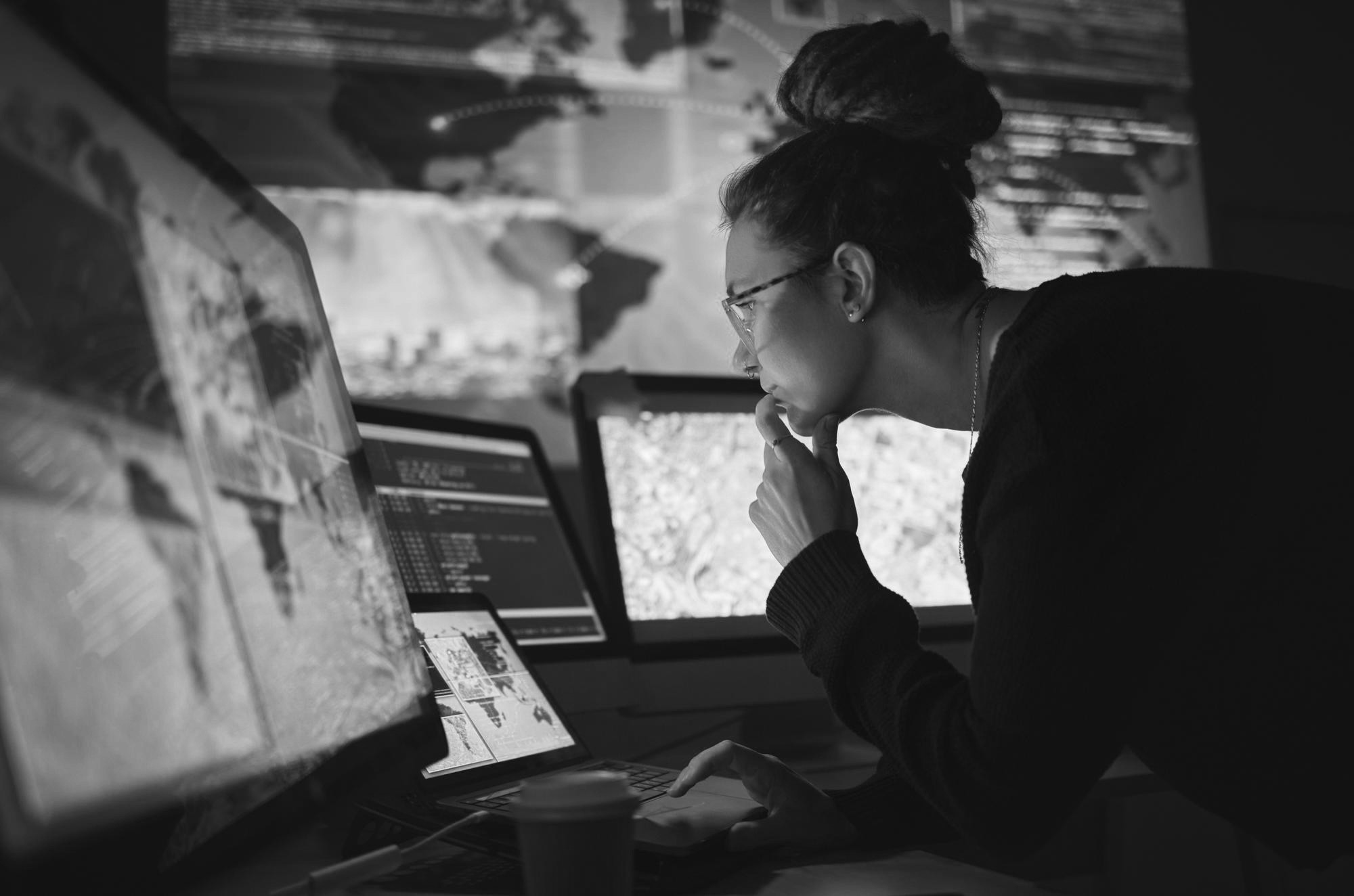 Woman analyzing data on multiple monitors, focused on screens with information.