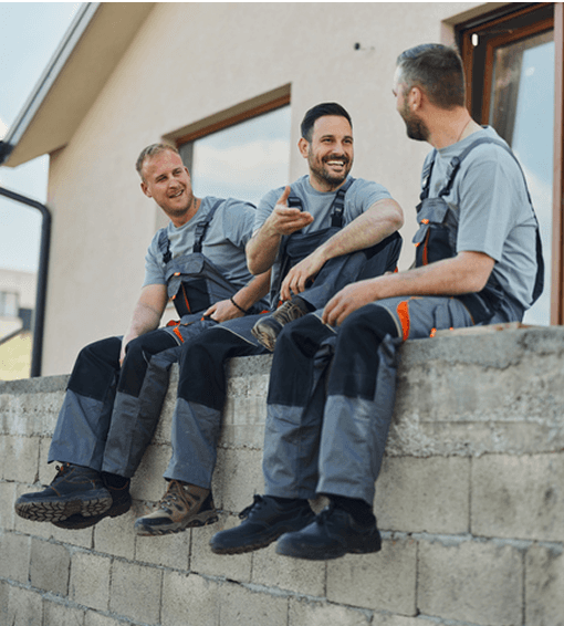 Ein Mann im blauen Hemd und verschränkten Armen lehnt sich an die Wand und schaut lächelnd in die Kamera.
