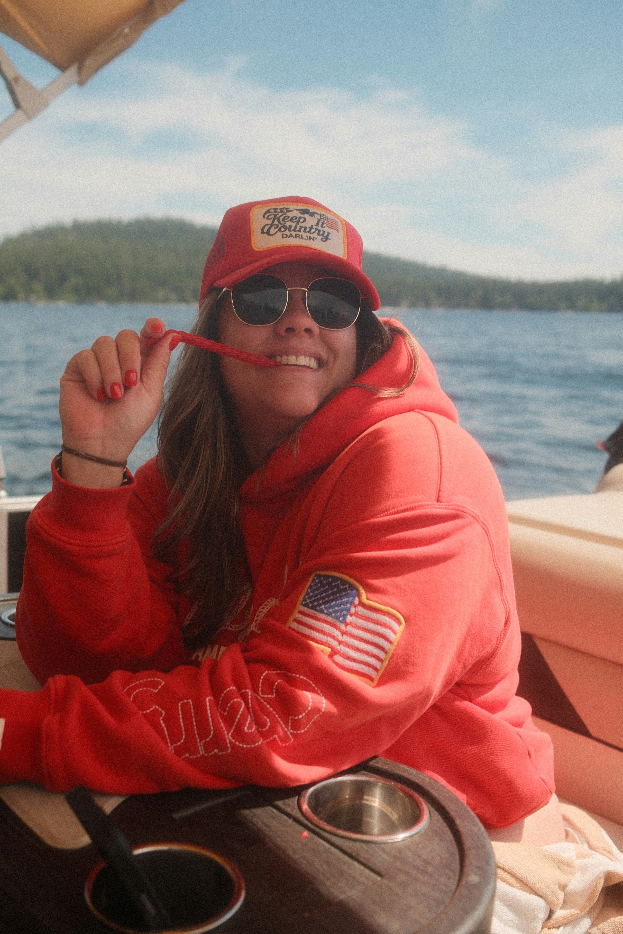 Smiling woman in red hoodie on lake.