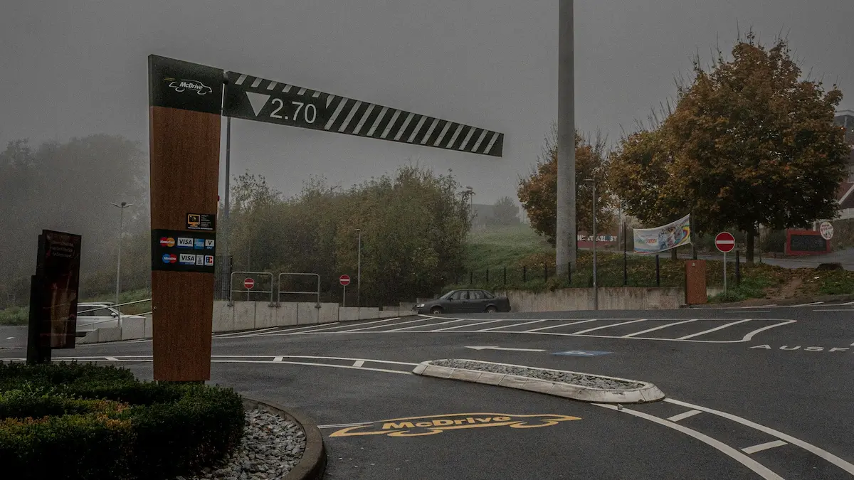A foggy and nearly empty drive-thru entrance on an overcast day, surrounded by quiet roads and muted autumn trees.