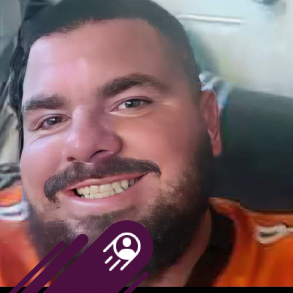 Close-up portrait of a freckled woman with soft pink hair and star earring, natural light, white tank top.
