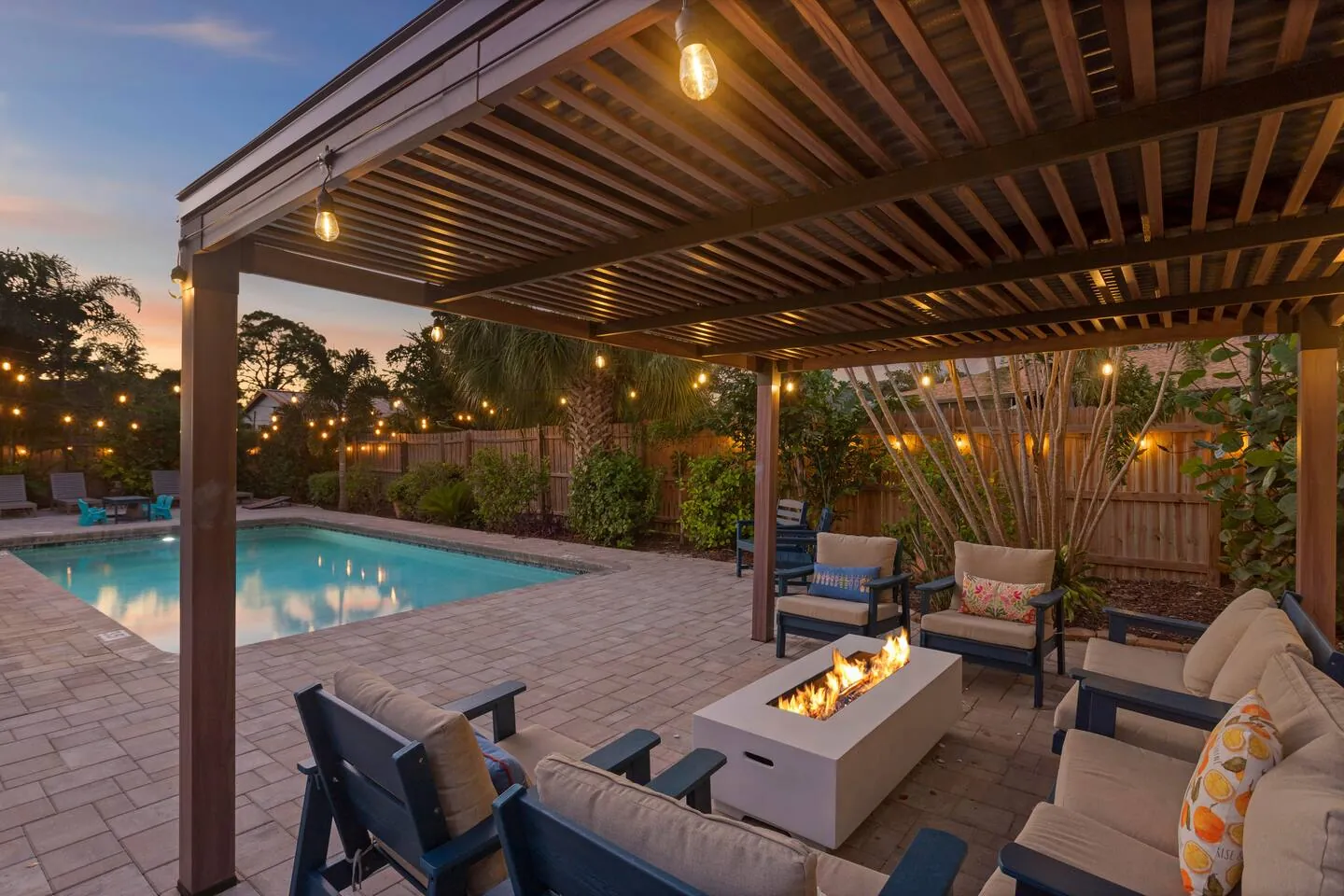 Pergola with fire table and lounge seating at dusk with pool behind at Sarasota Beach Bungalow, Bradenton, Florida