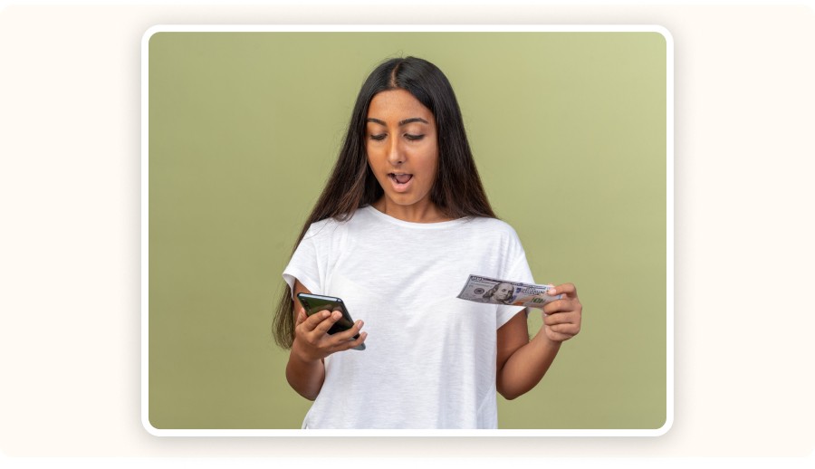 Surprised woman holding smartphone and dollar bill, checking money or payment&nbsp;