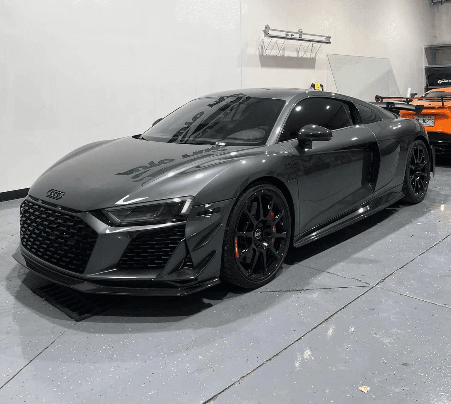 A sleek gray Audi R8 sports car is parked indoors on a polished concrete floor.