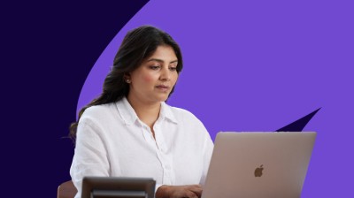 Woman working on a laptop against a purple branded background.