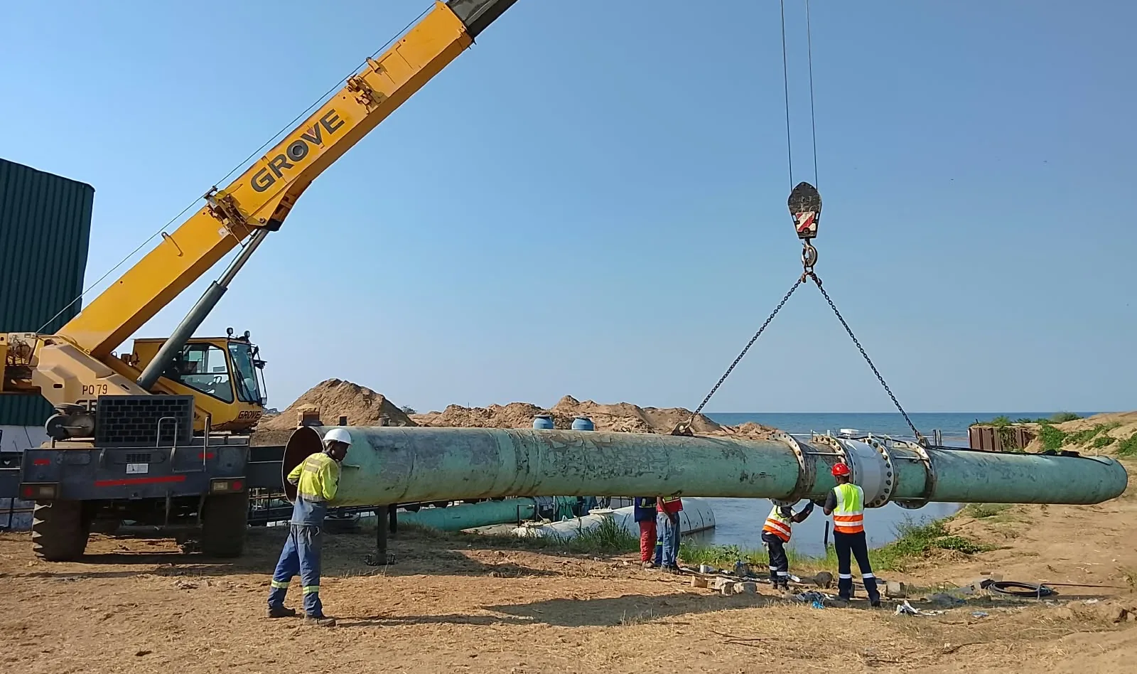 Site crew installing a large-diameter steel water main with a mobile crane