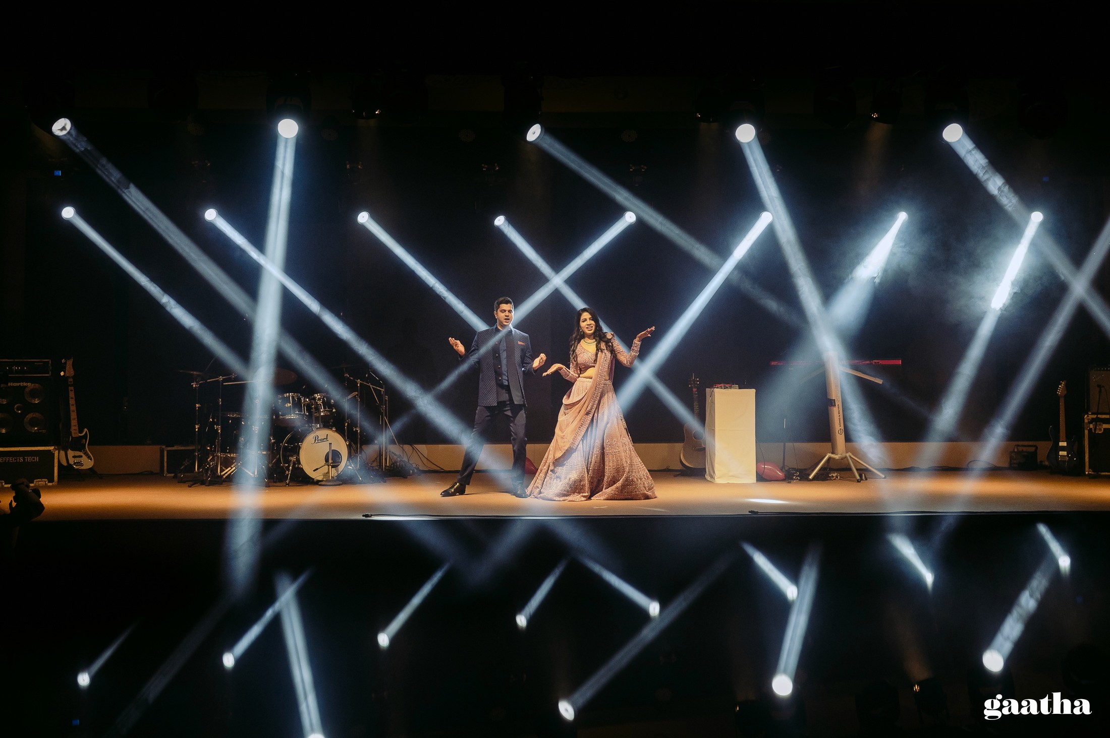 A person in an apron uses a wooden peel to place a freshly baked loaf of artisan bread into a rustic, wood-fired oven, with a flickering fire visible inside, set against the backdrop of a sunlit kitchen.