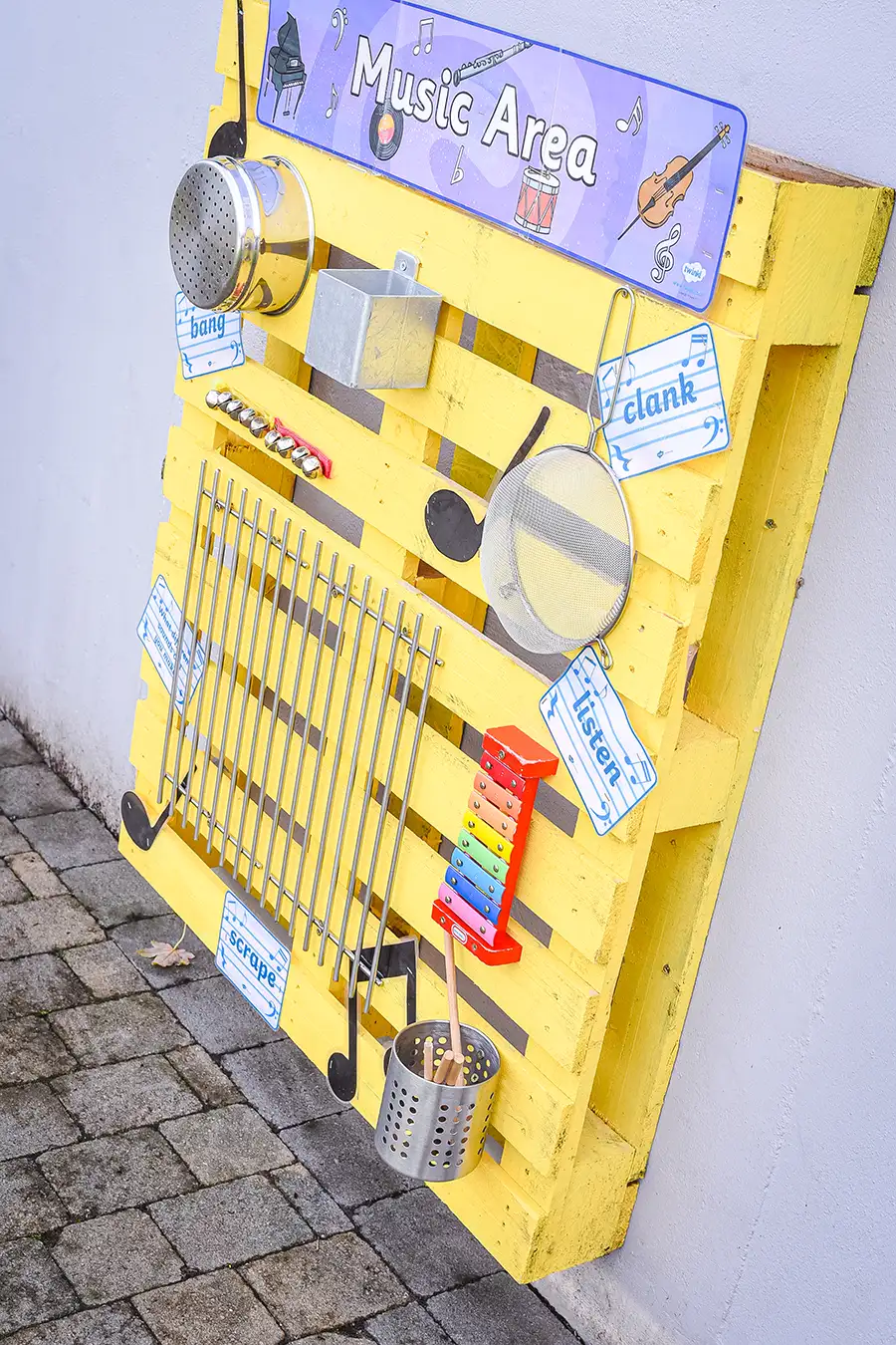 DIY outdoor music station made from a bright yellow pallet with various instruments like shakers, drums, and xylophone.