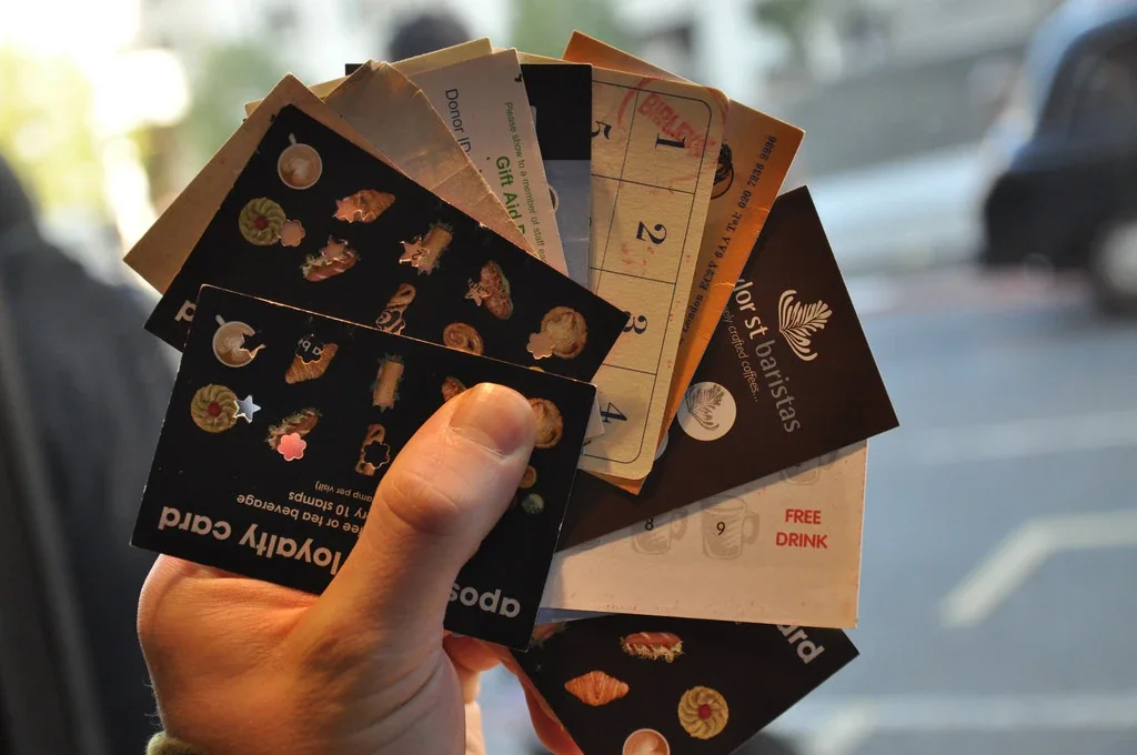 Hand holding fanned paper punch cards with food items and "FREE DRINK" offer visible outdoors.