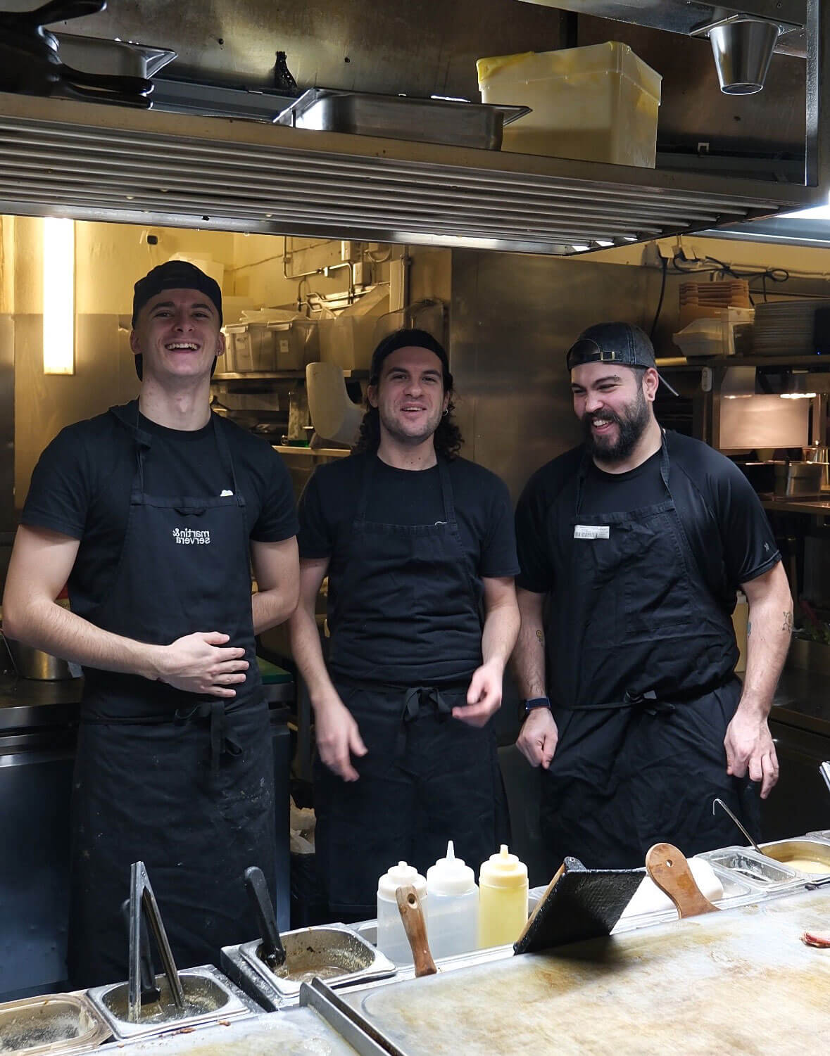 Three chefs standing in the Greasy Spoon kitchen smiling.