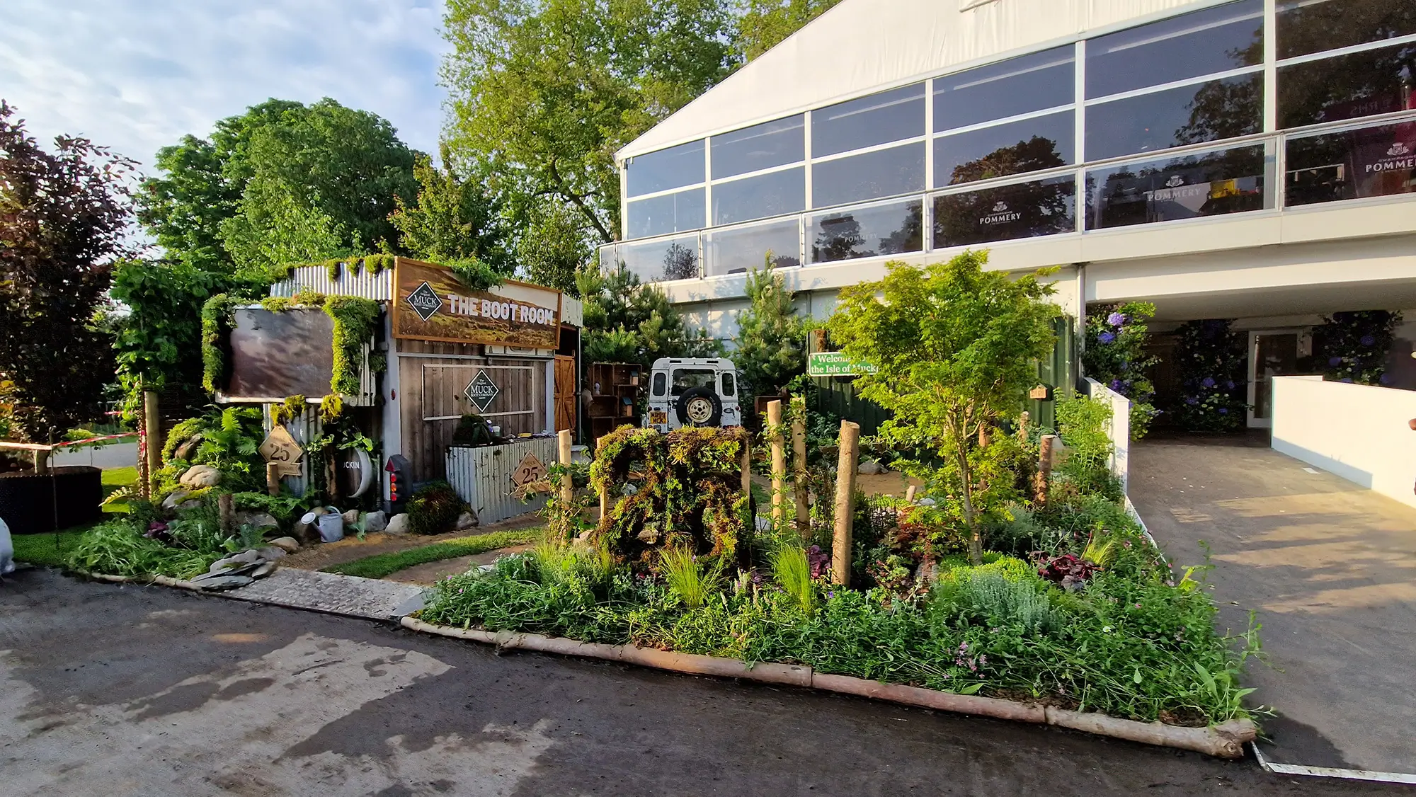 A well-maintained garden with various plants and a glass-fronted building in the background.