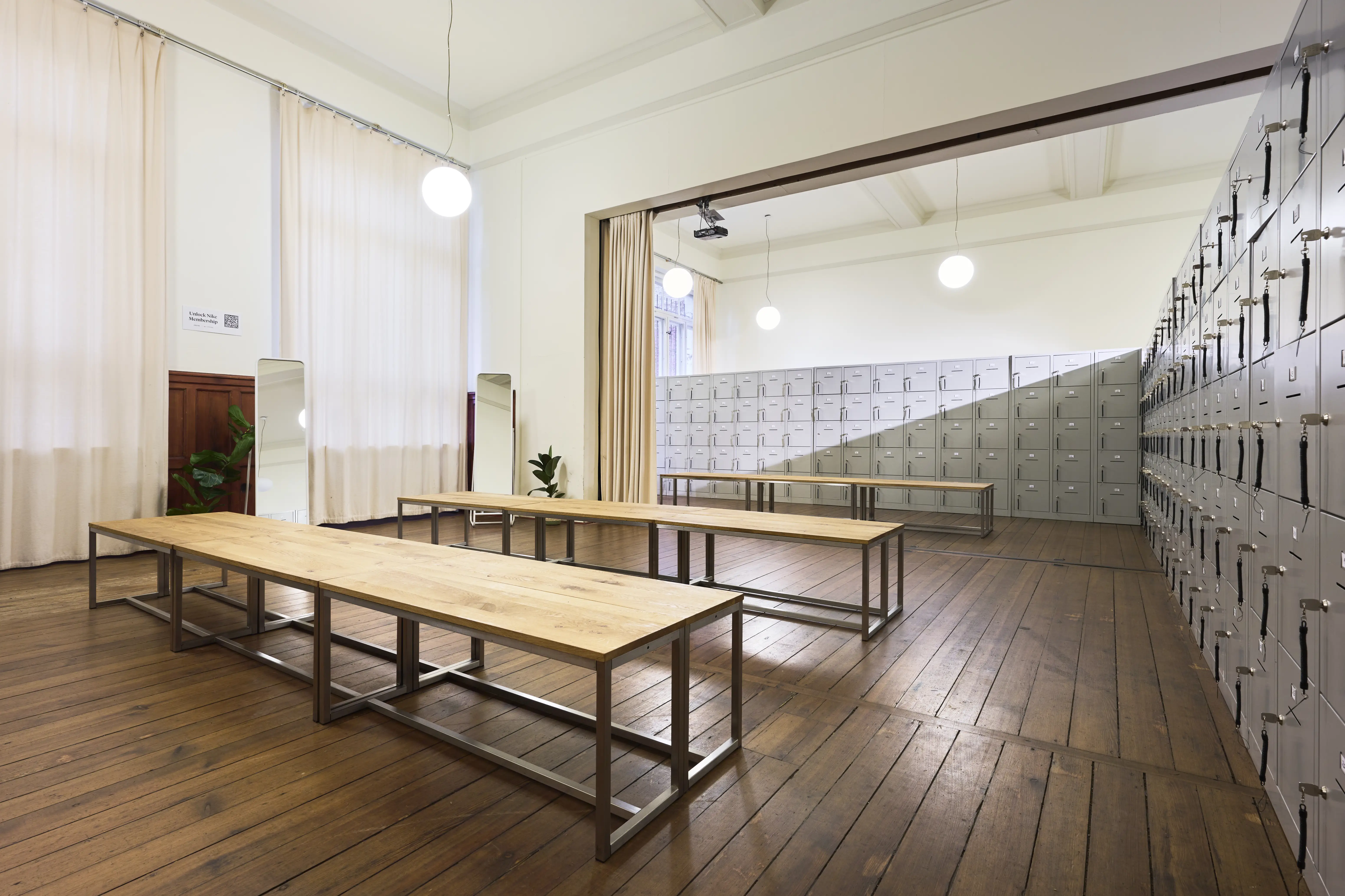 Changing room with grey locker walls, wooden benches and round pendant lights.