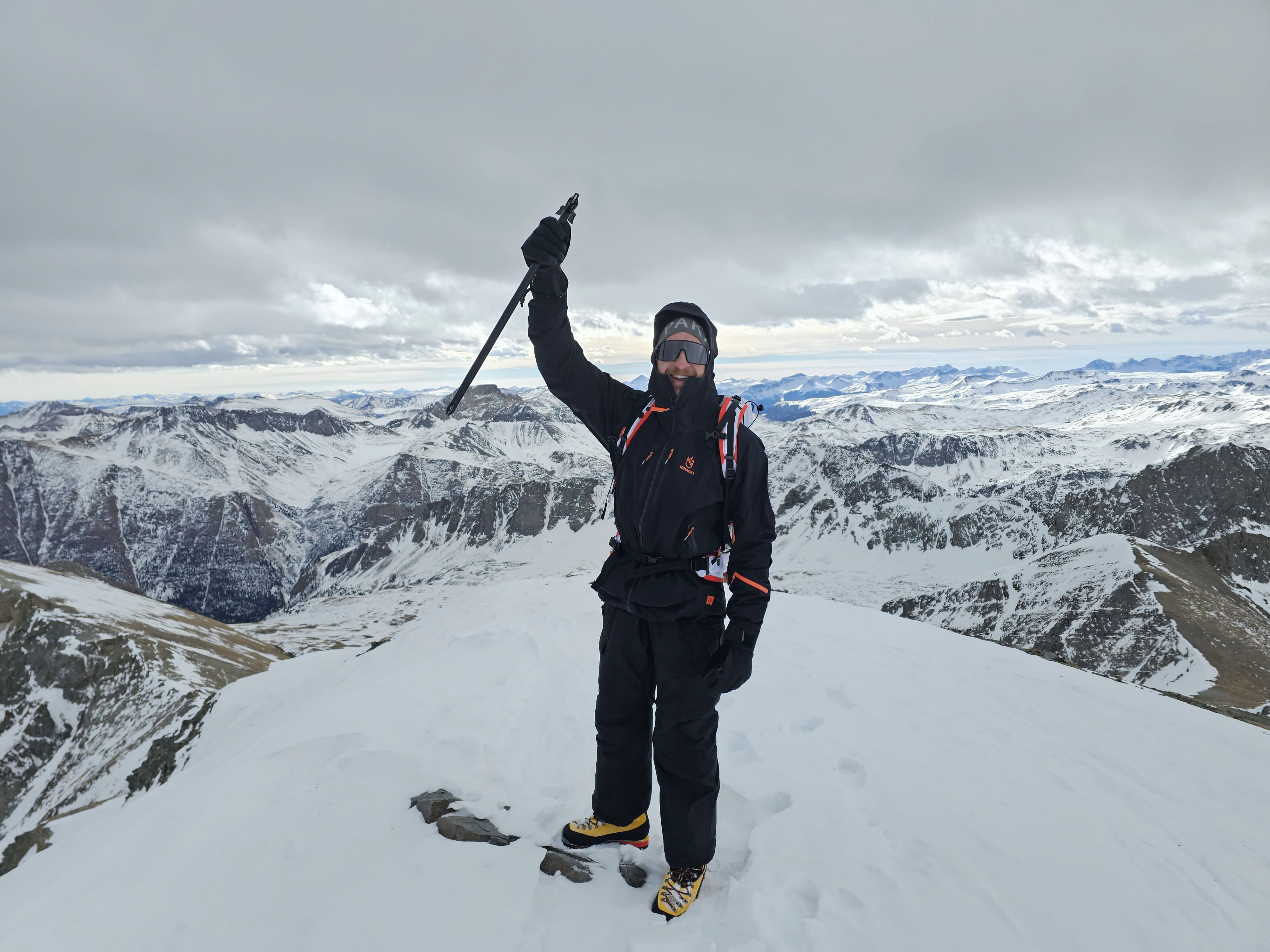 Climber raises their ice axe in triumph on their first 14er summit in winter