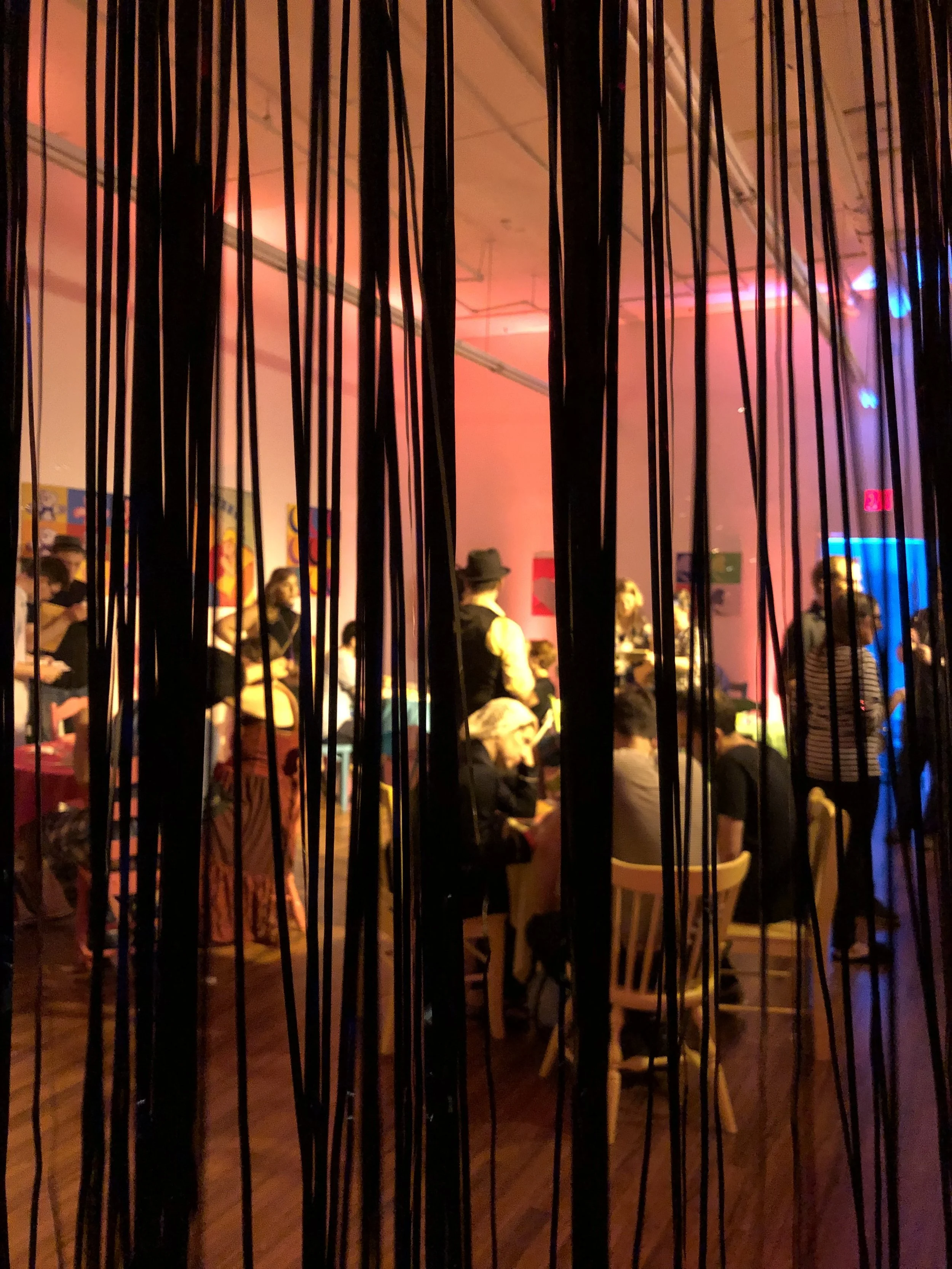 A view through hanging strands into the warmly lit Night Cafe.