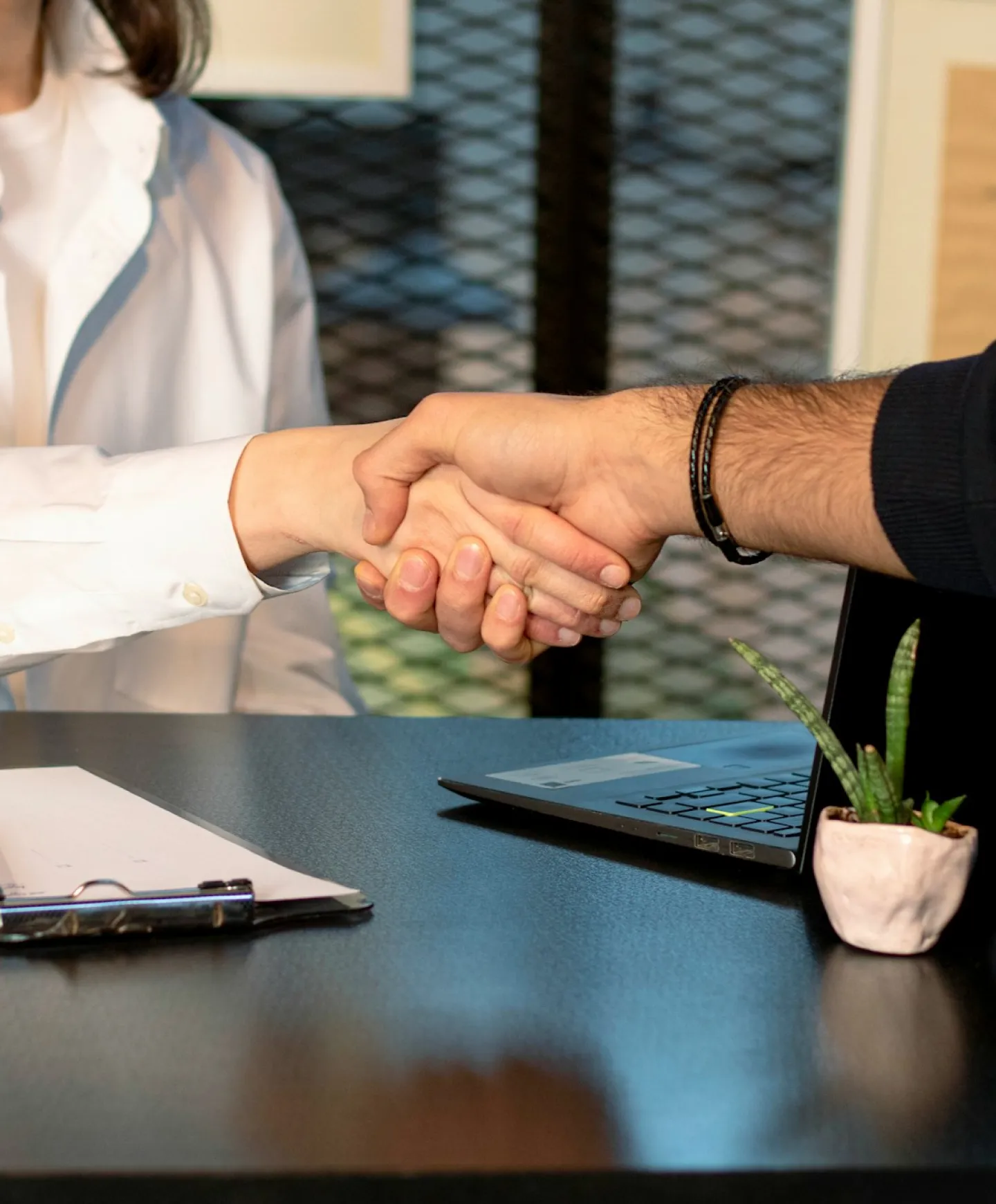 Two people shaking hands over a desk