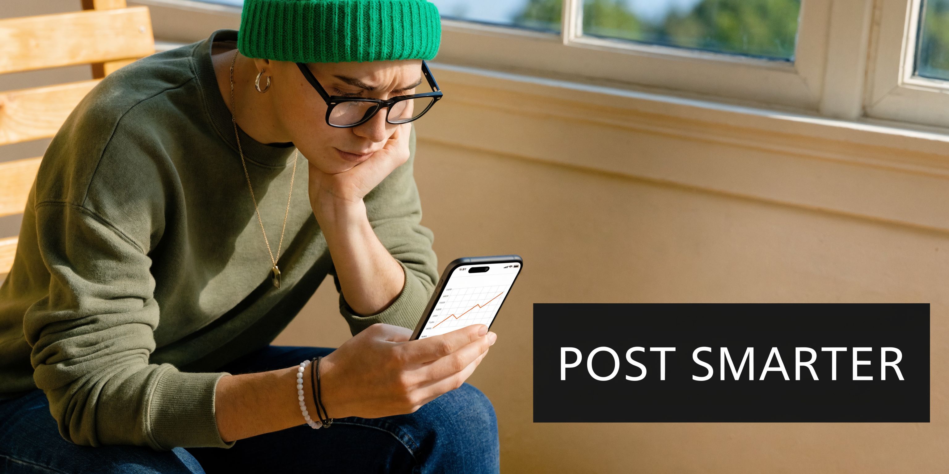 A person in a green beanie and sweater looking closely at stock market charts on a smartphone.