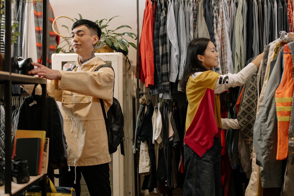 Clienți care aleg haine într-un magazin second-hand, ilustrând revânzarea în regimul marjei de TVA pentru bunuri second-hand