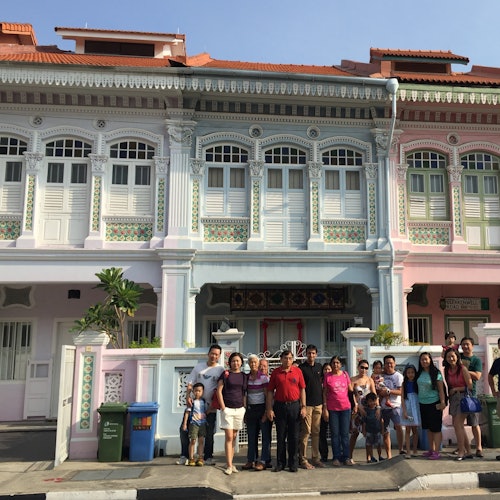 A group of people stands in front of colorful two-story houses with ornate trim and shutters under a clear sky.