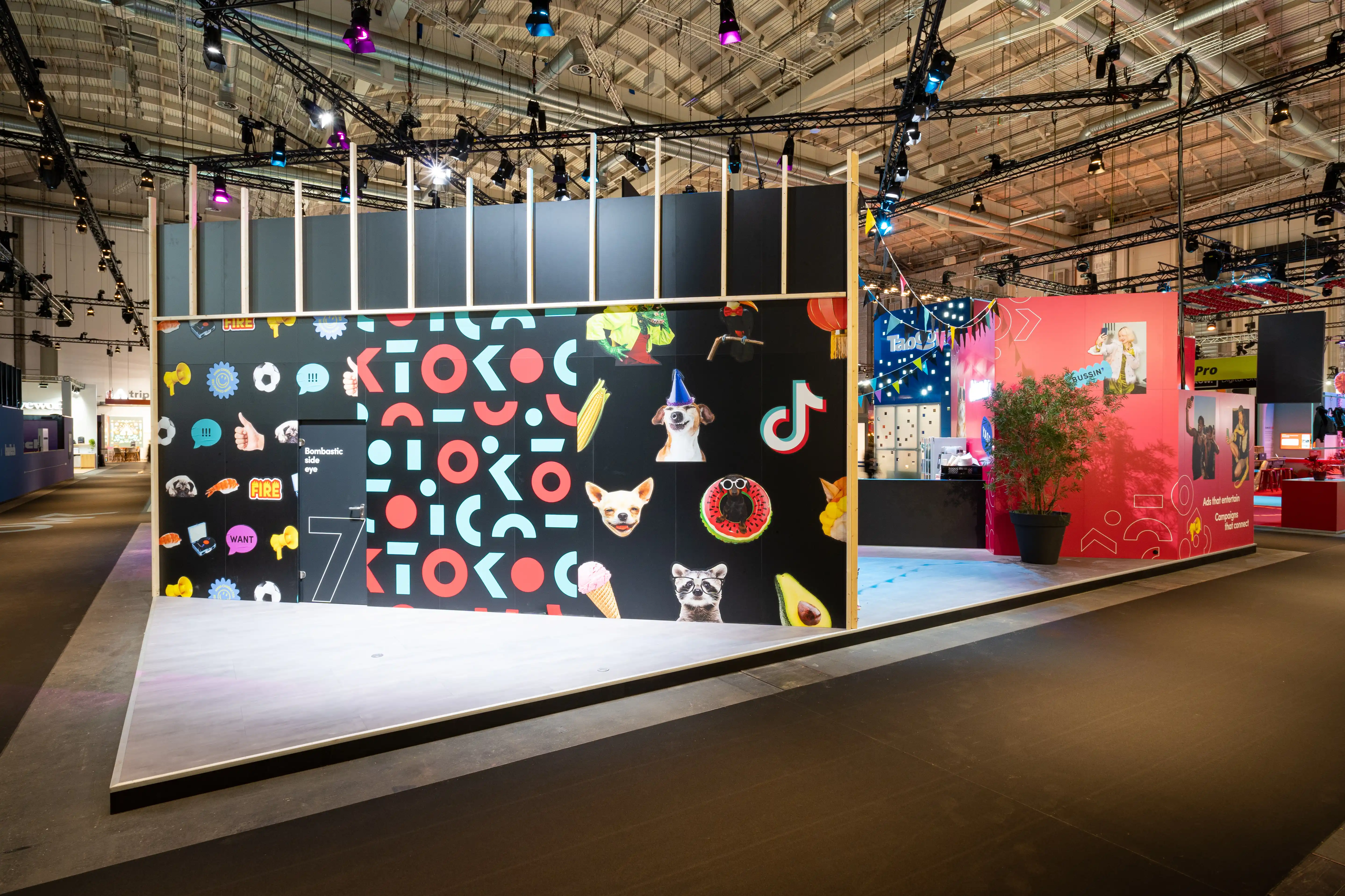 Back wall of the TikTok booth with playful sticker collage of animals, emojis and graphic shapes on black ground.