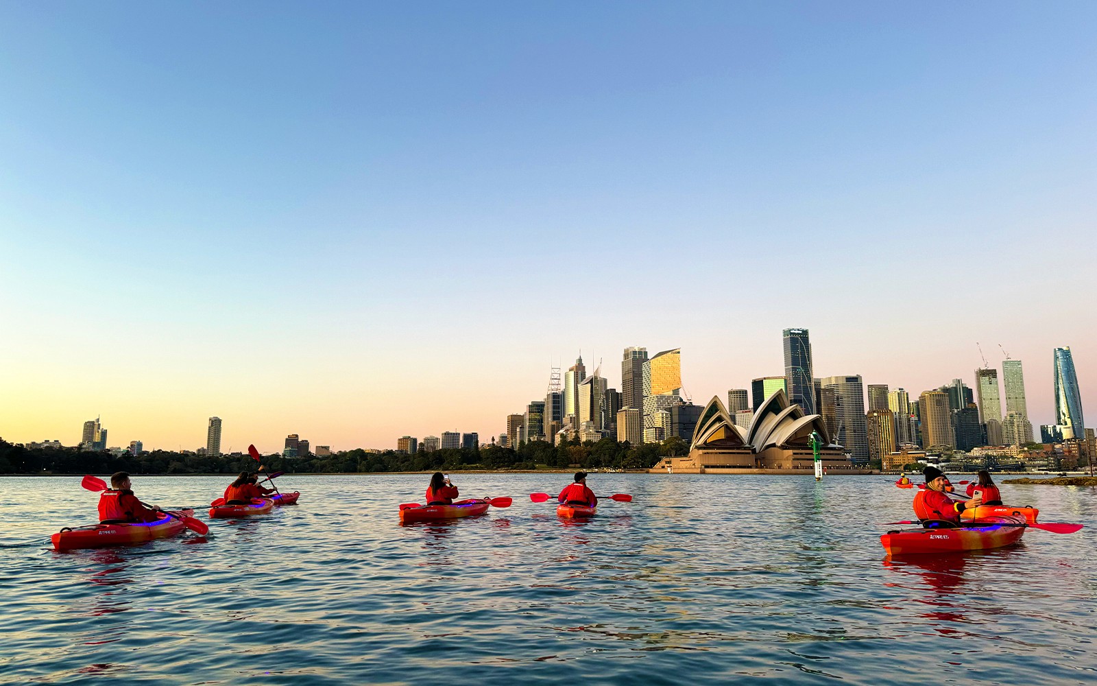 一群人在悉尼港享受皮划艇之旅，背景是著名的悉尼歌剧院，提供可選早餐服務