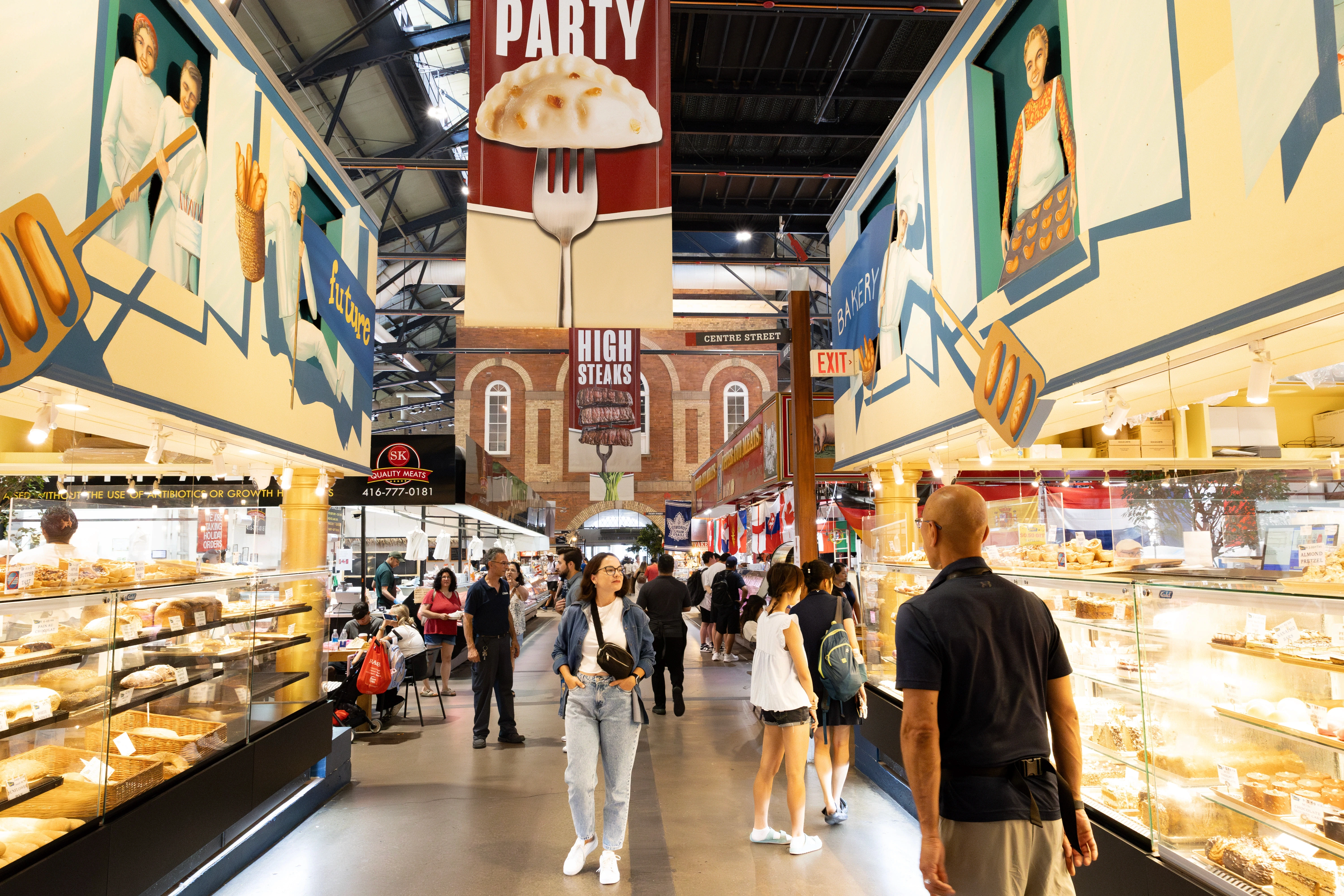 Pessoas caminhando e conhecendo o St. Lawrence Market, com bancas de comida e ambiente movimentado.