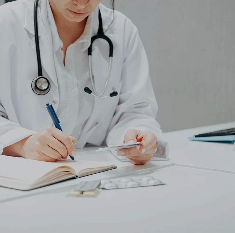Healthcare professional in a white coat reviewing medical notes and medication at a desk