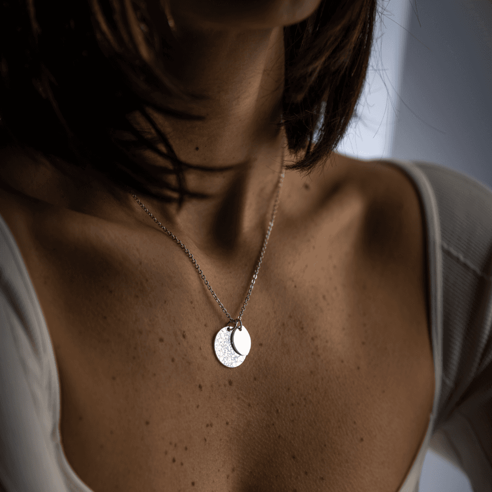 A woman wearing a three-quarter silver Night Sky Moon Phase pendant layered on top of a bigger Night Sky Star Map Silver pendant.