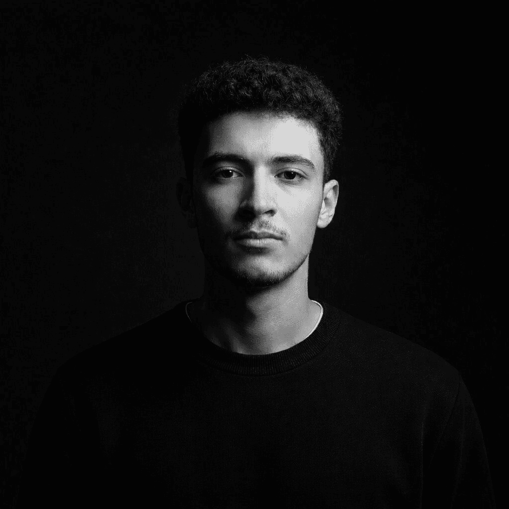 A thoughtful young person with dark hair gazes to the side, captured in soft black and white lighting.