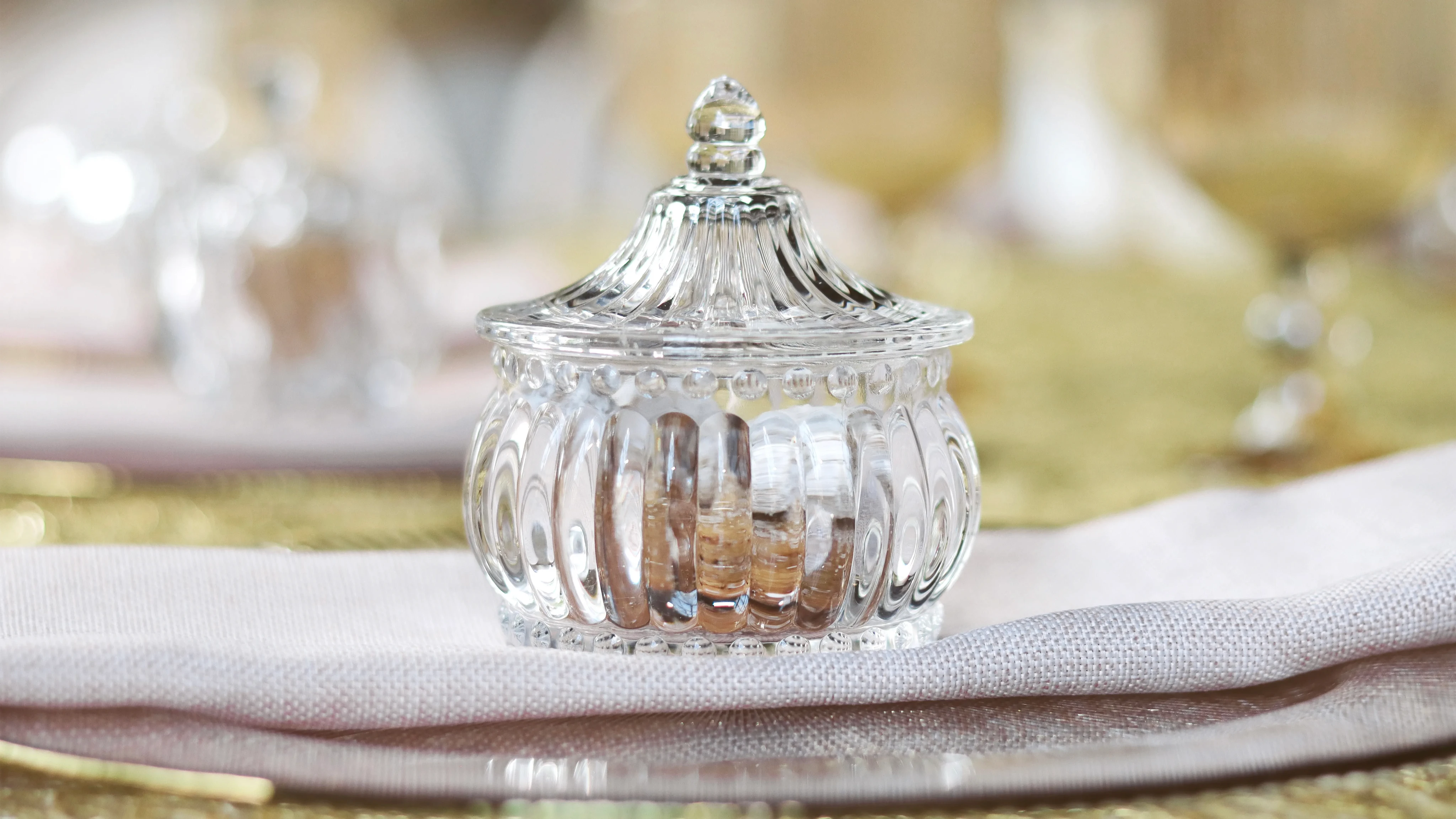 Detalle de frasco de cristal sobre mantel dorado y rosa