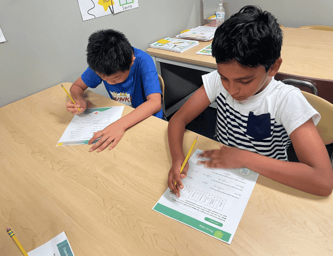 Two boys doing math problem-solving worksheets at a table