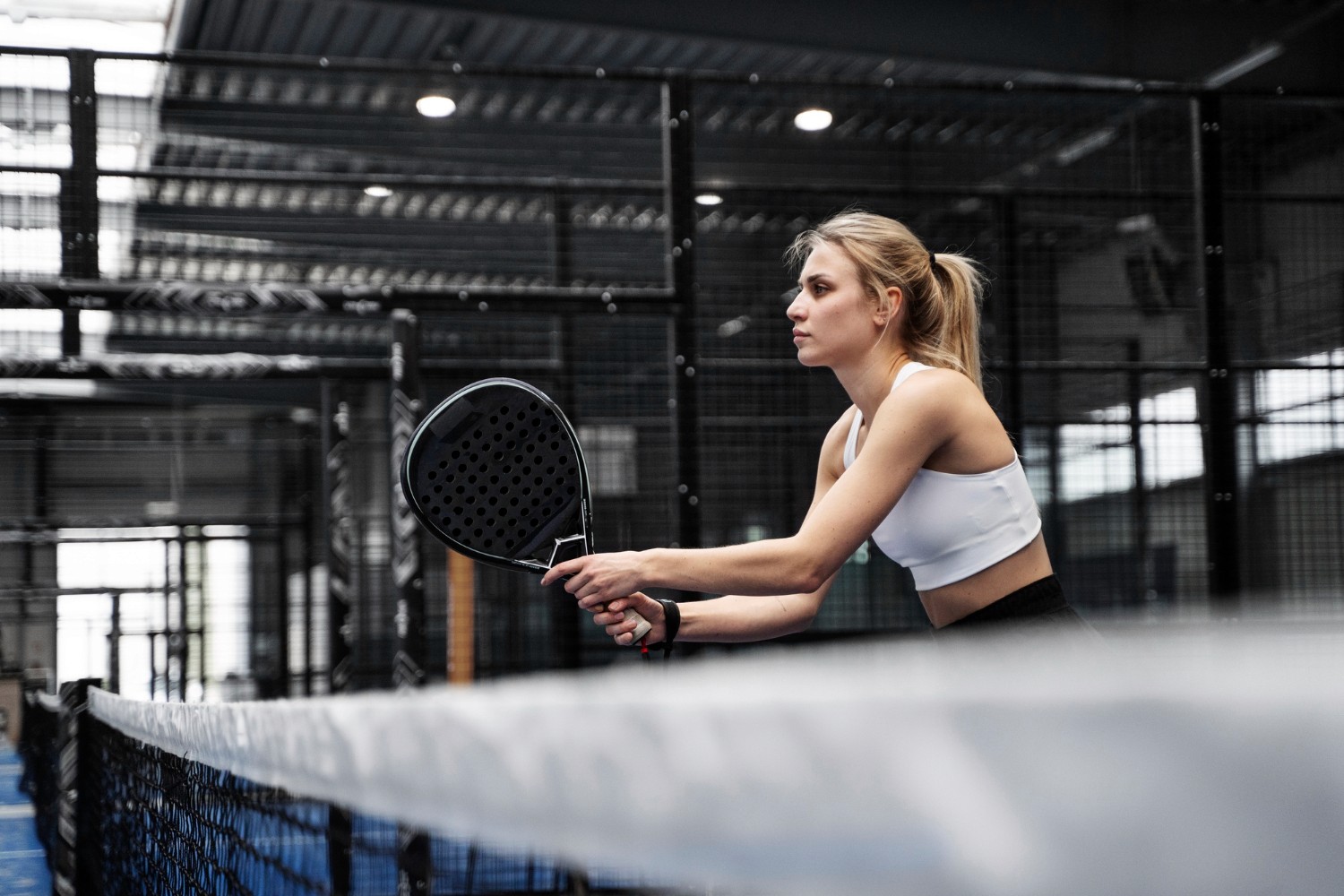 Jugadora de pádel golpeando la pelota en una pista indoor, imagen representando las experiencias regalo de Padel Pro Camp