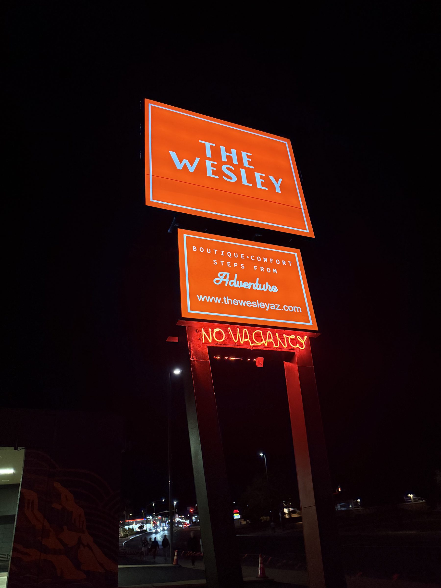 The Wesley roadside sign lit at night, orange panels reading The Wesley and Boutique Comfort Steps From Adventure above a red neon No Vacancy sign.