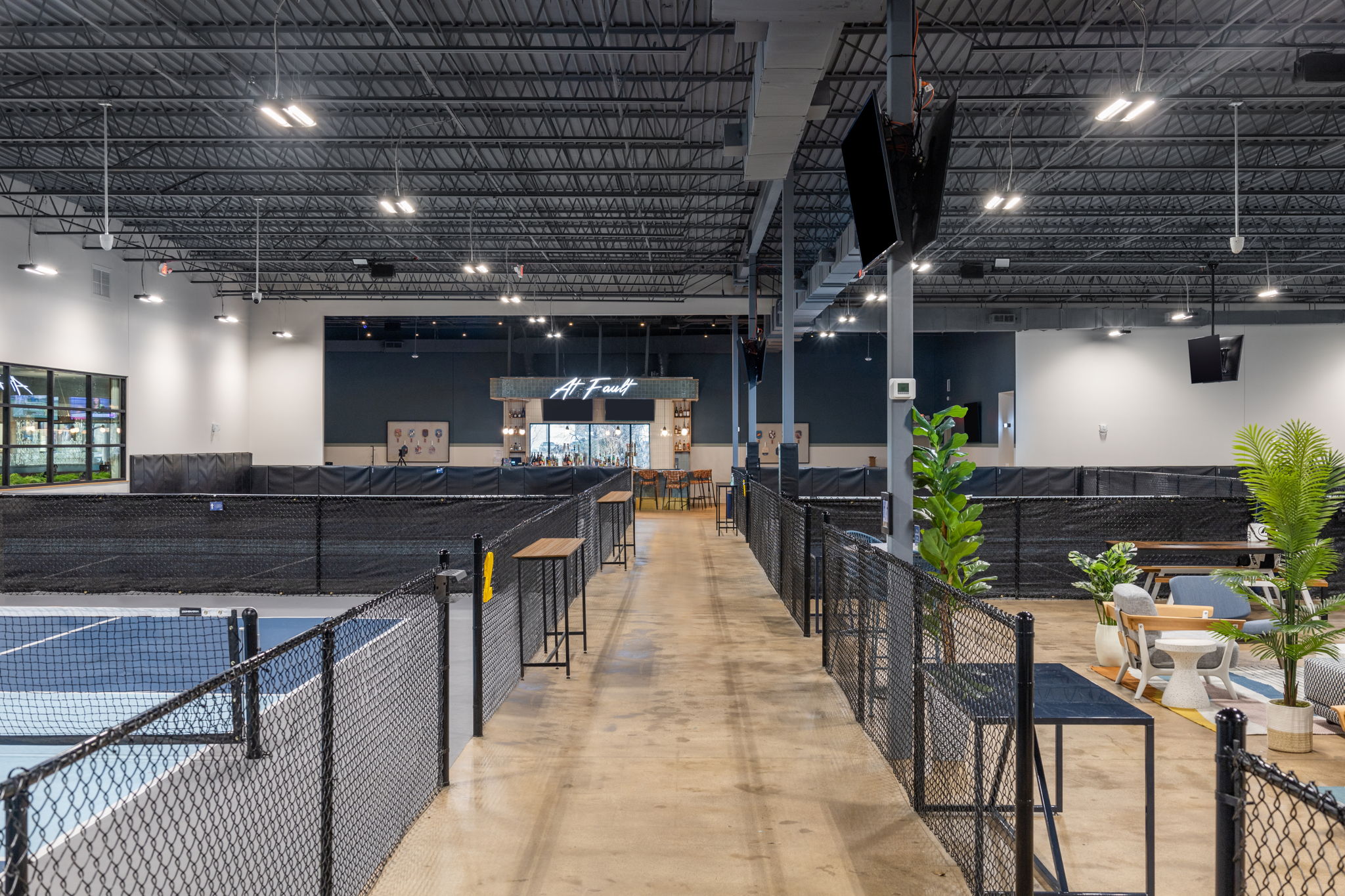 Wide interior view of At Fault pickleball venue showing indoor courts, central walkway, wayfinding layout, and illuminated bar signage in Dallas, Texas.