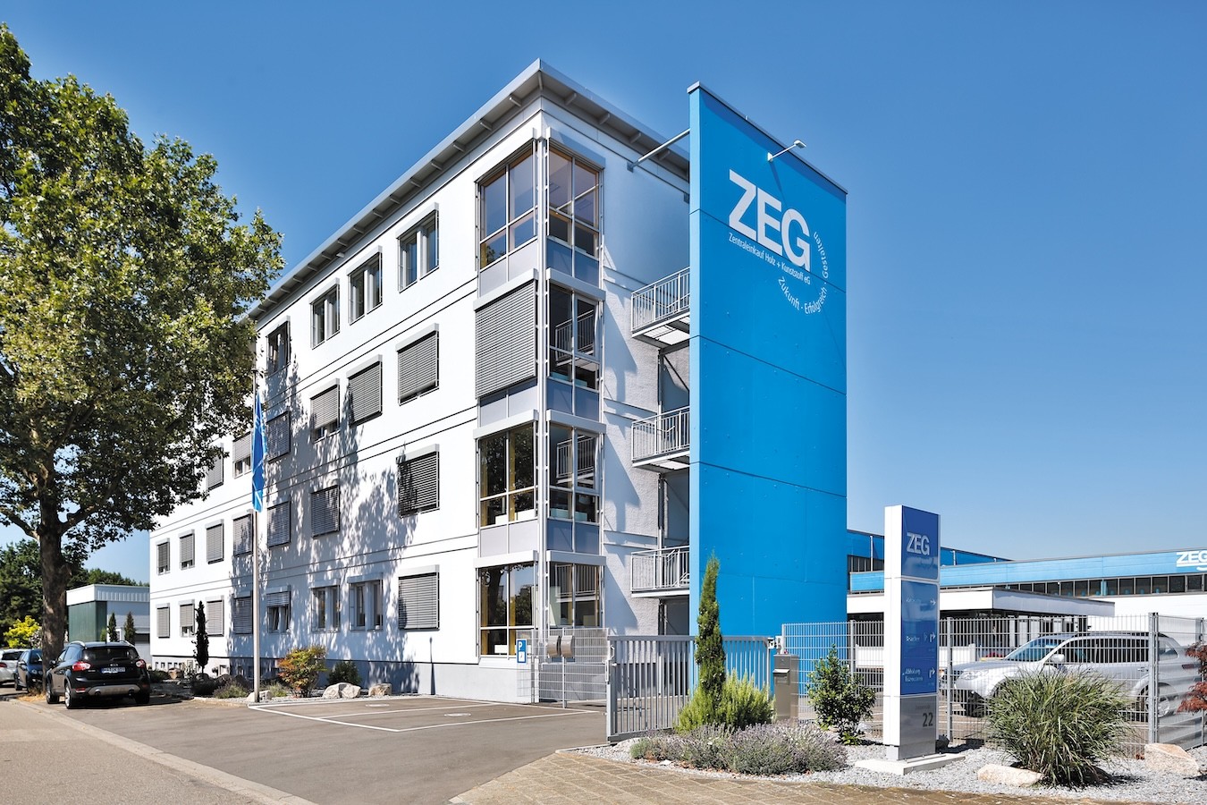 ZEG Zentraleinkauf Holz - + - Kunststoff eG in einem modernen Bürogebäude mit großer blauer Fassade unter klarem Himmel.