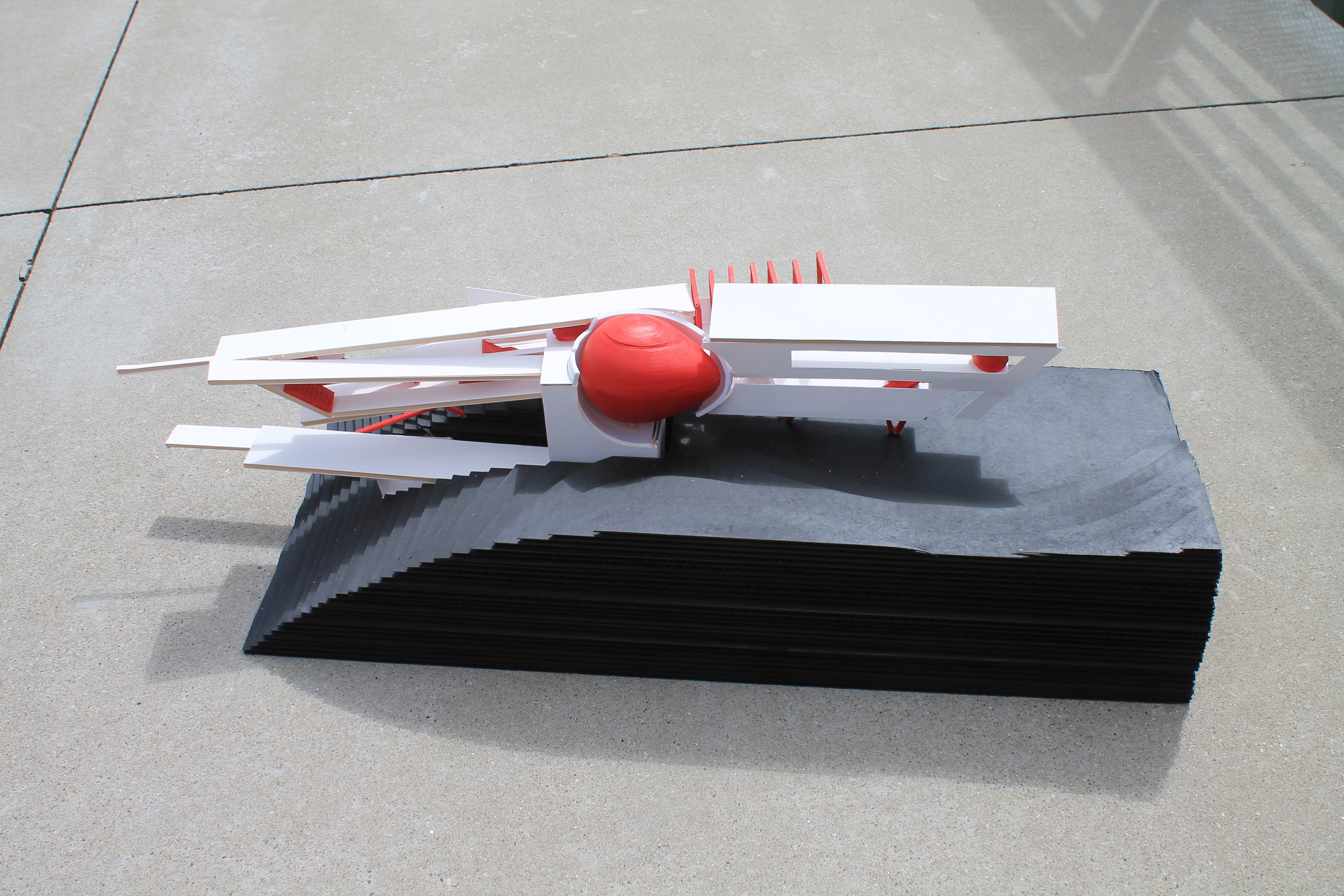 Side view of a white angular architectural model with linear platforms and a red spherical volume above a dark contoured site base.