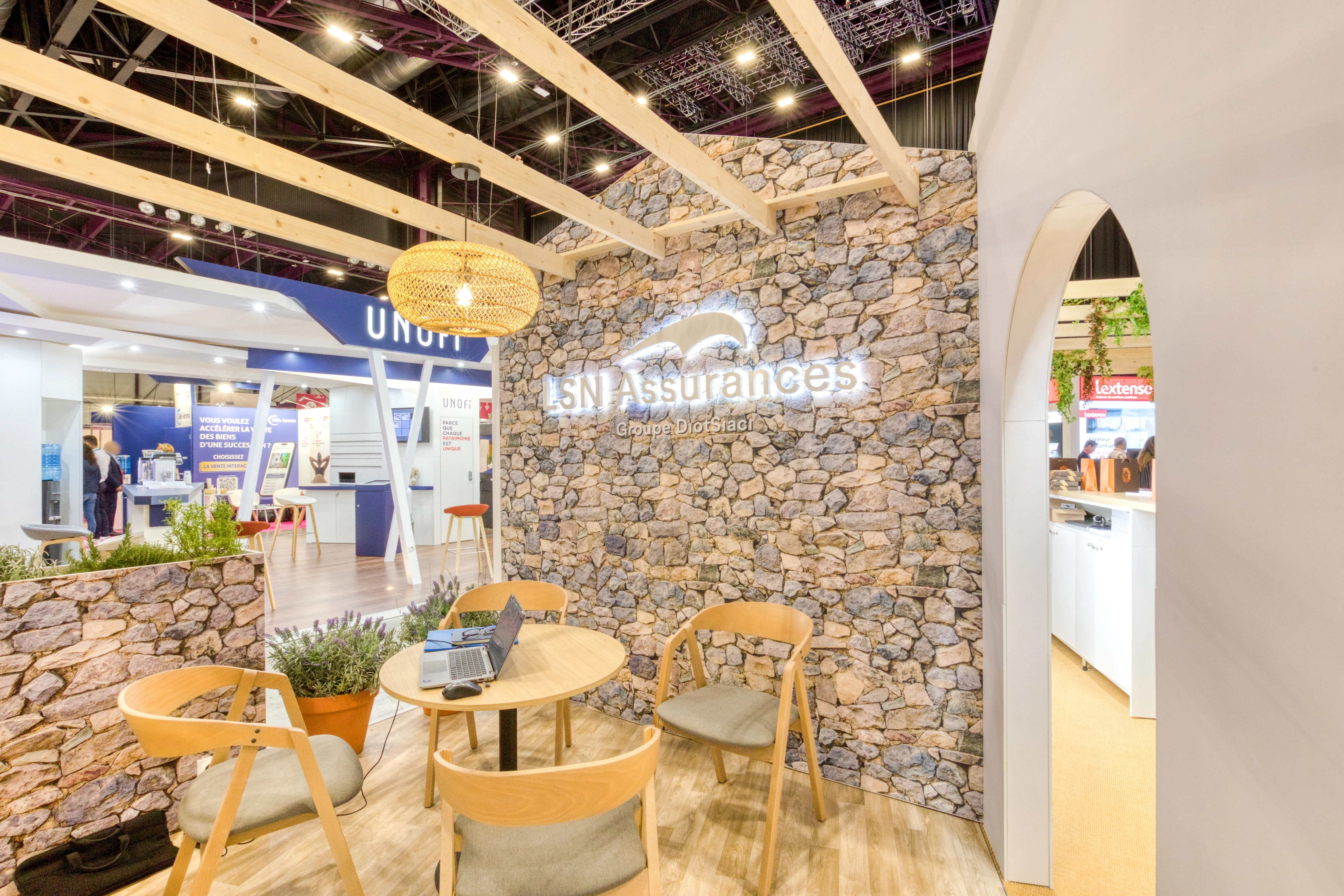 « Espace d’échange LSN Assurances avec murs en pierre et mobilier en bois, stand conçu par Expace »