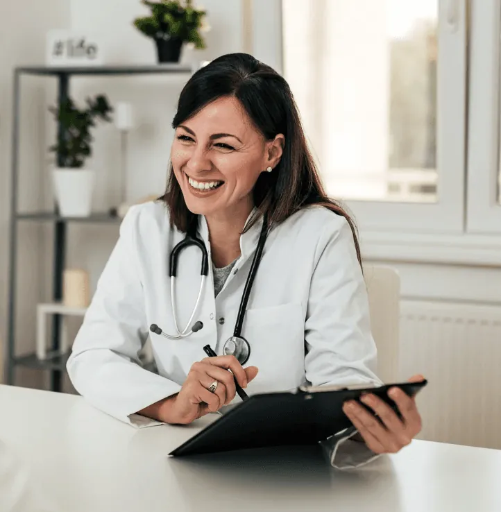 Smiling female family doctor at TejoMed clinic in Lisbon sitting at her desk with a stethoscope and tablet, representing personalized concierge healthcare and patient-centered care.