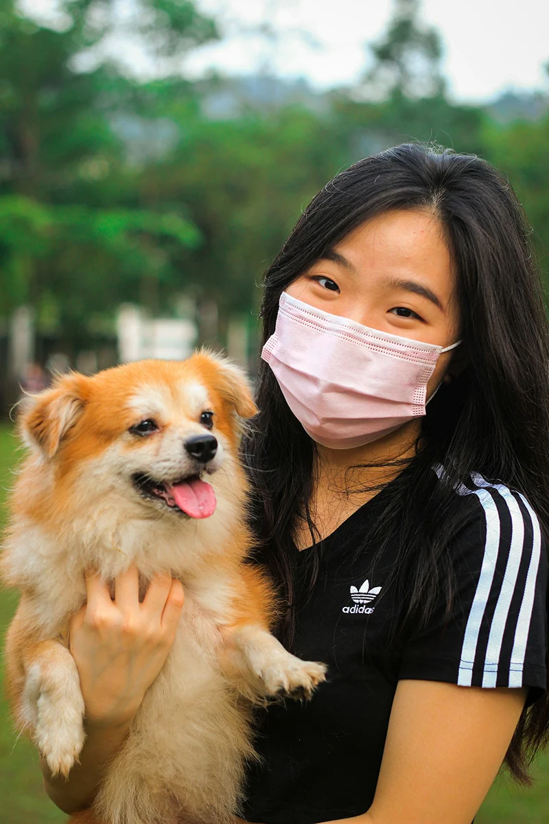 Woman outdoors holding a small tan dog