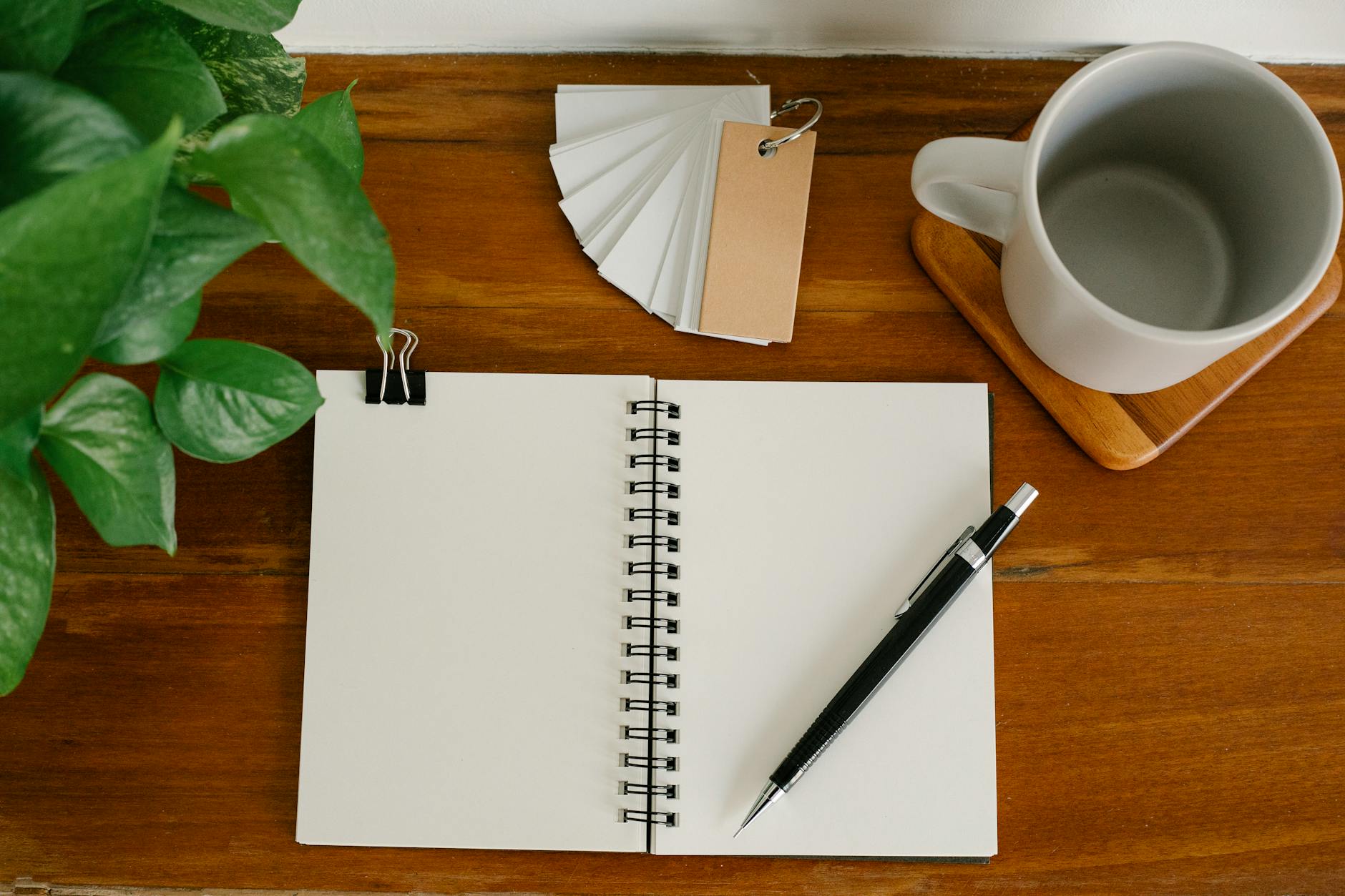 Close-up of a wooden desk featuring an open digital planner, a cup of coffee, and a pair of glasses.