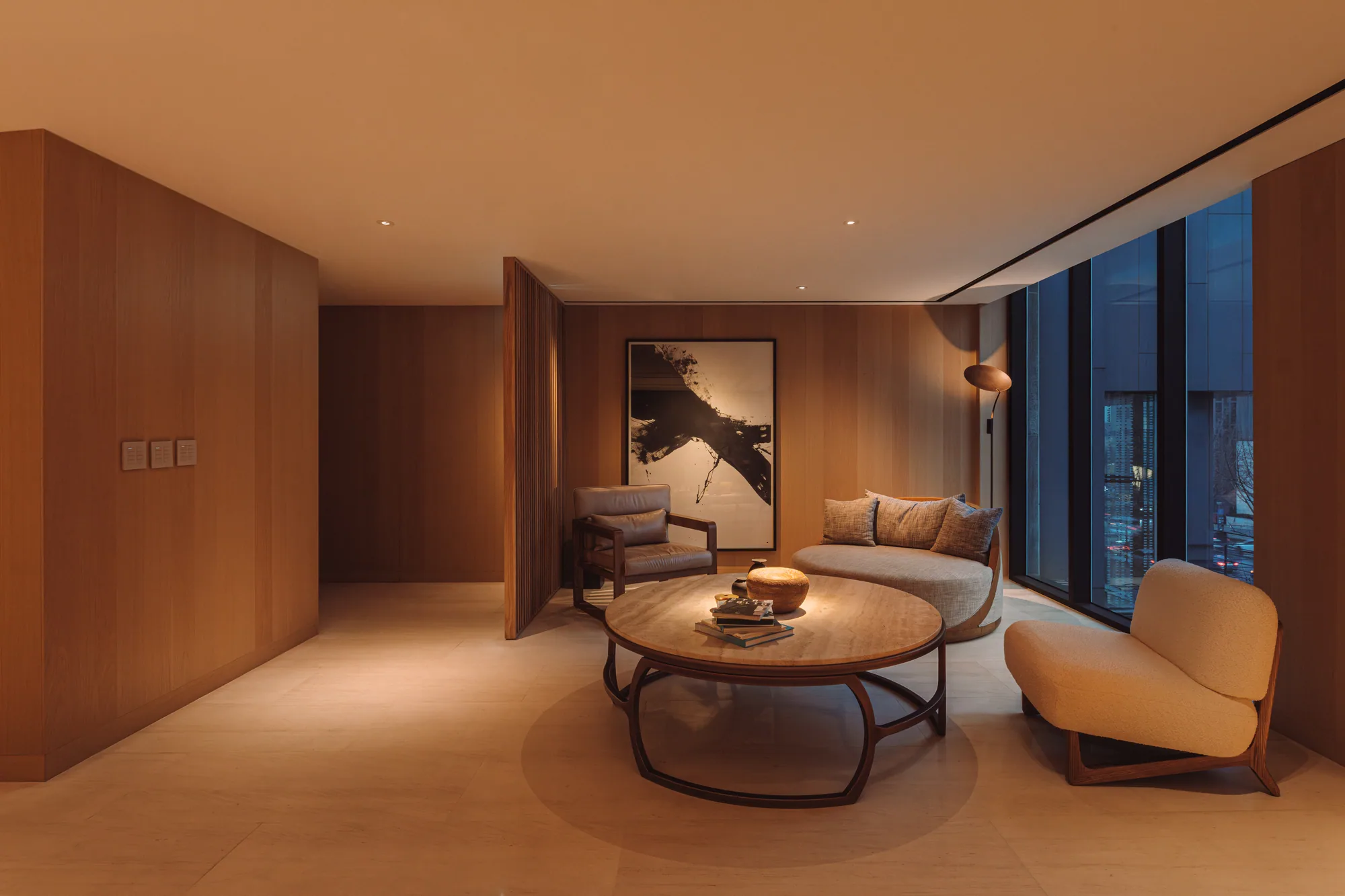 A third-floor PLAYA private room, sofa and lounge chair set by a window over the evening city